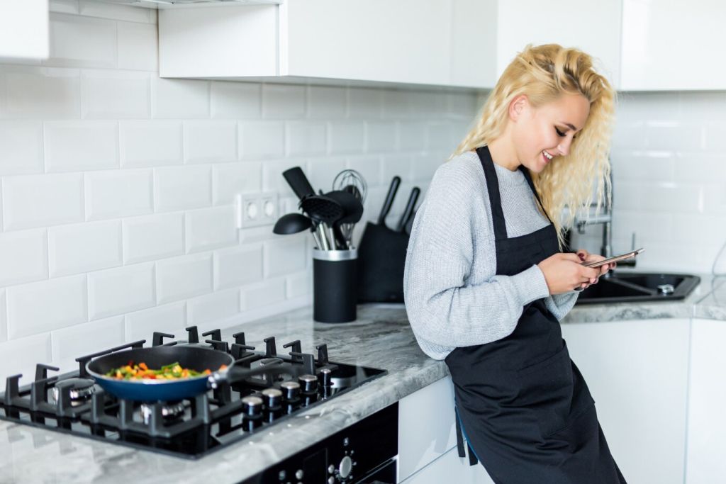 beautiful-blonde-girl-cooking-food-in-frying-pan-use-on-the-mobile-phone-and-smiling-while-cooking-in-kitchen-at-home_231208-1425.jpg